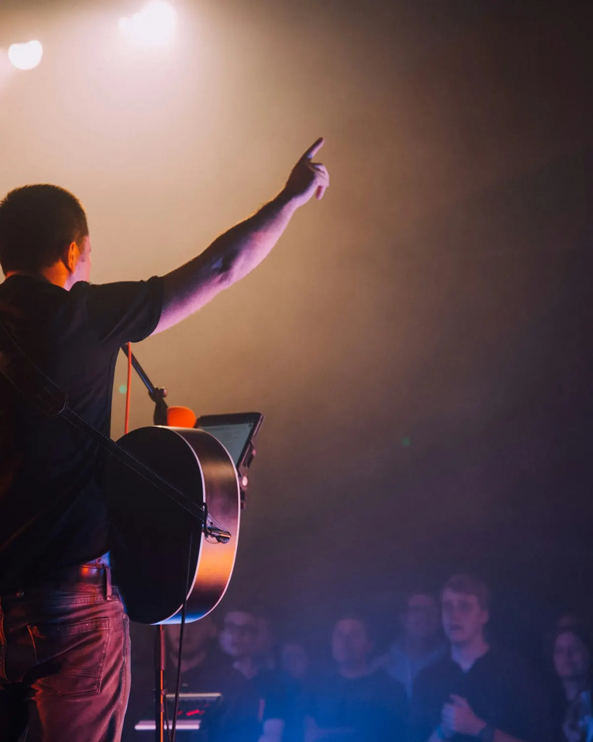 A worship leader with a guitar raising a hand toward the congregation
